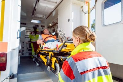 Paramedics in uniform putting injured man on stretcher in ambulance
